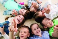  Kinder liegen auf dem Boden mit den Köpfen zu einander. Sie lachen und strecken die Arme nach oben.